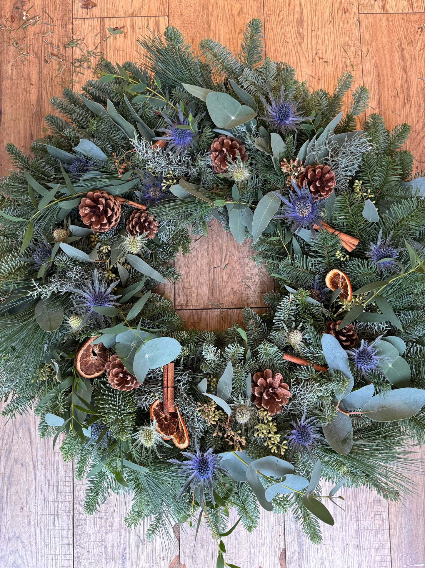 Close-up of blue Sea Holly, pinecones, and cinnamon in handmade Christmas wreath – Barns Florals Cornwall